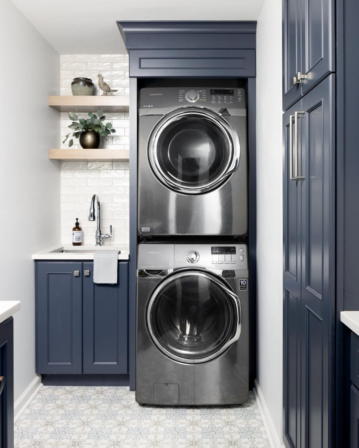 Navy blue cabinets and stacked silver washer dryer in a modern laundry room.