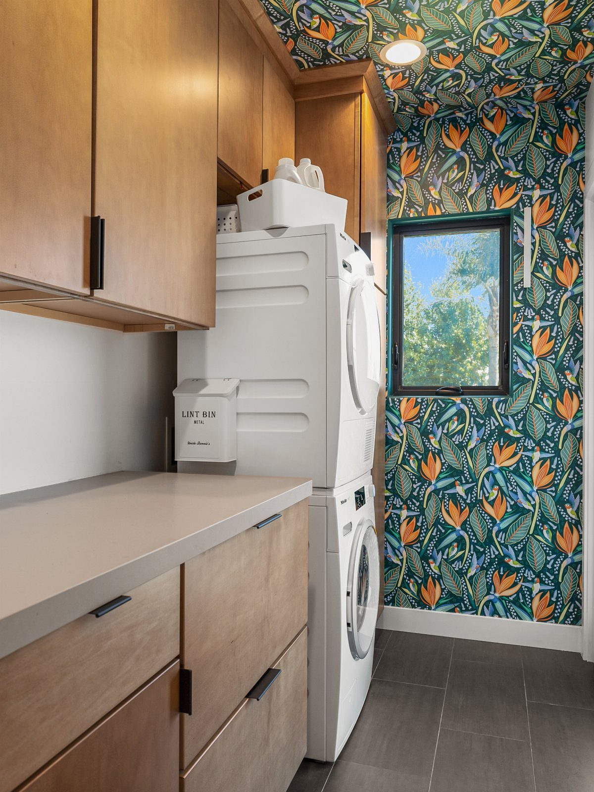 Stacked white washer and dryer next to vibrant tropical leaf patterned wallpaper.