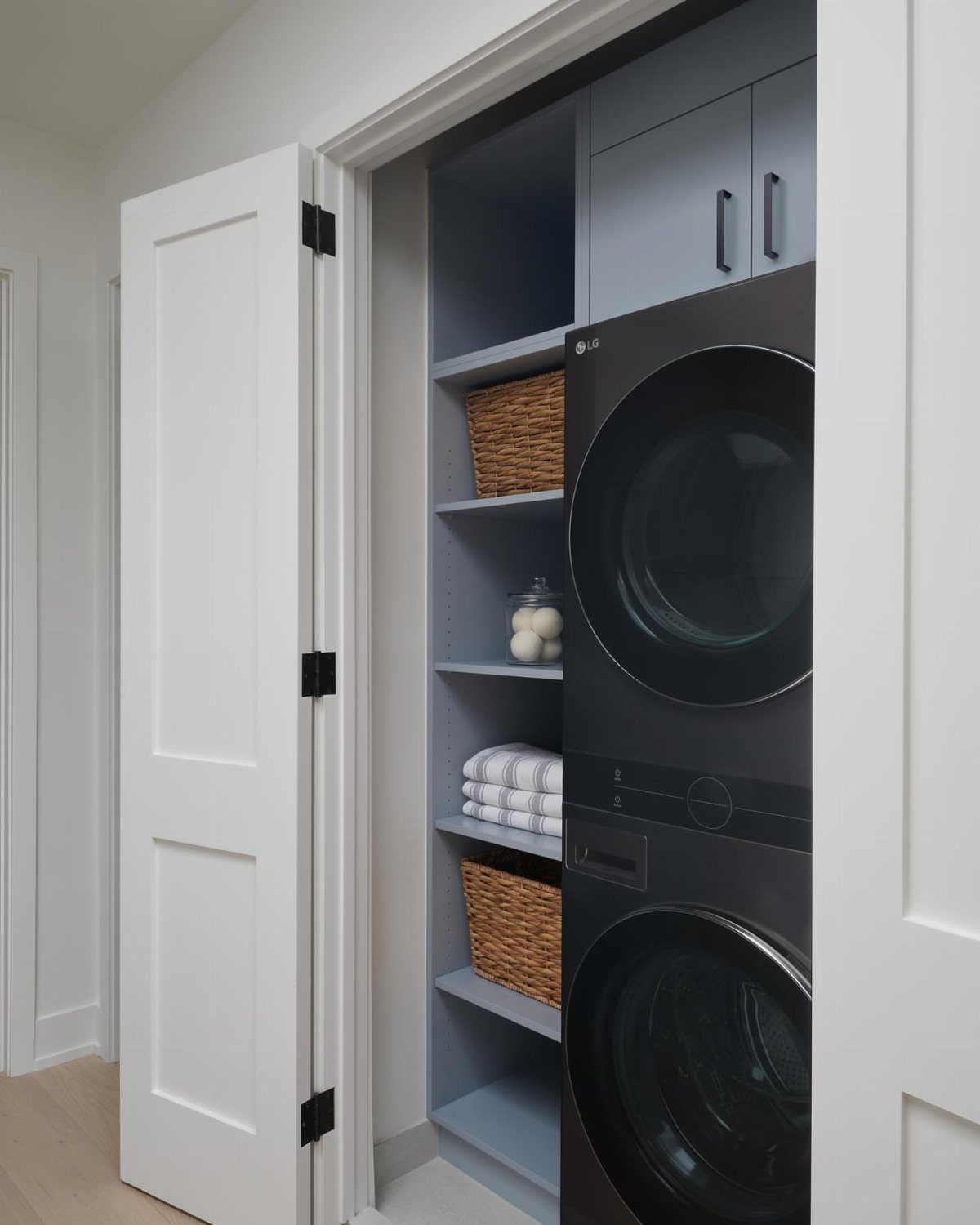 Stacked black washer and dryer in a grey laundry closet with open shelving
