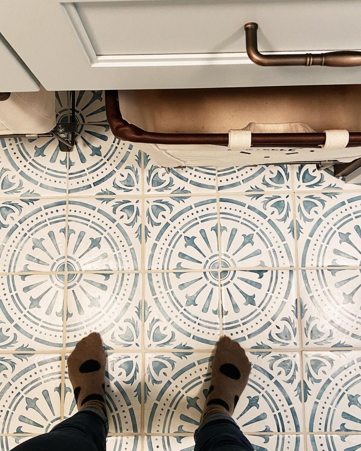 Patterned blue and white floor tiles with a person's feet in brown socks.