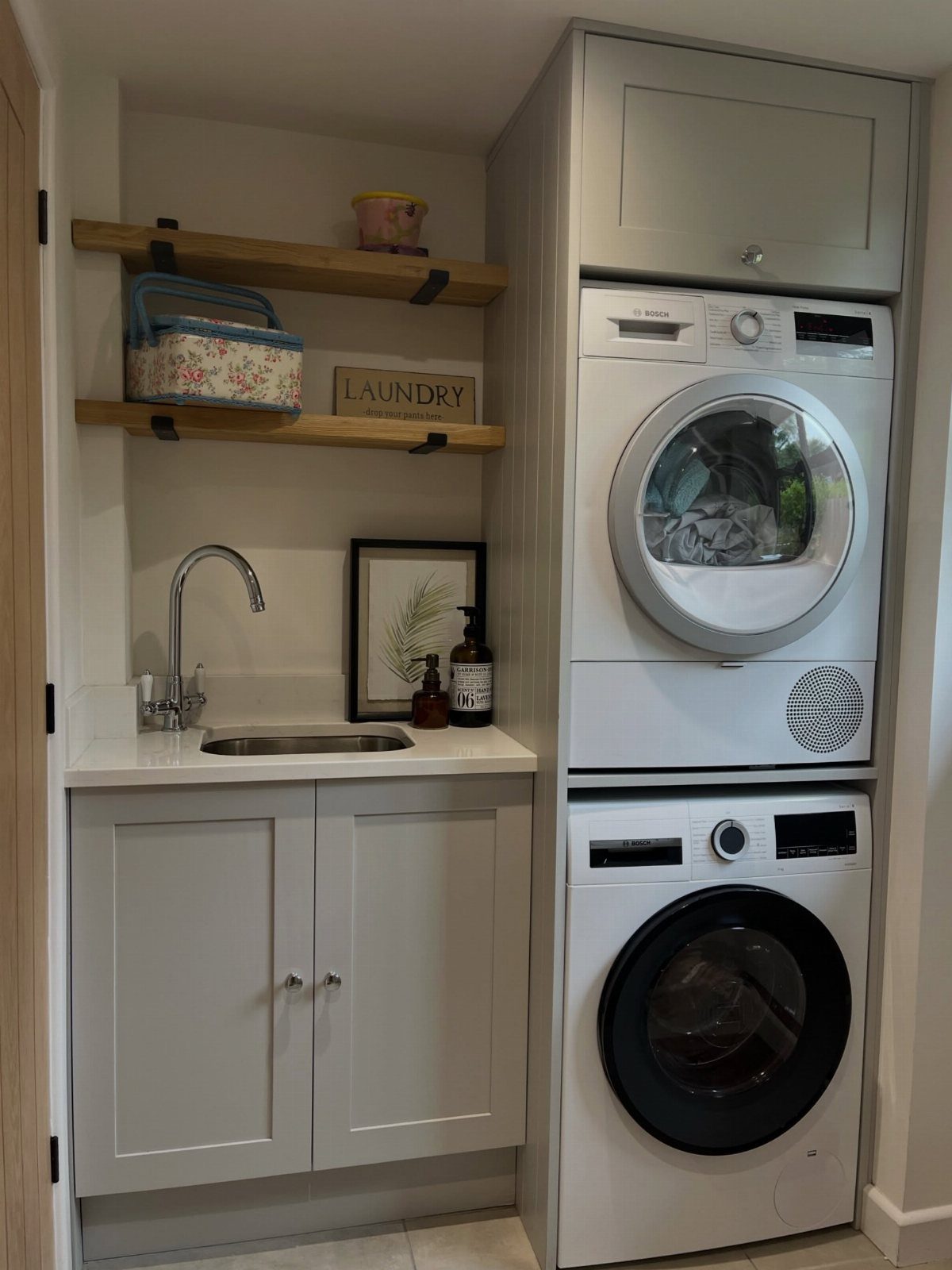 Stacked white washer and dryer next to a sink and wooden shelves.