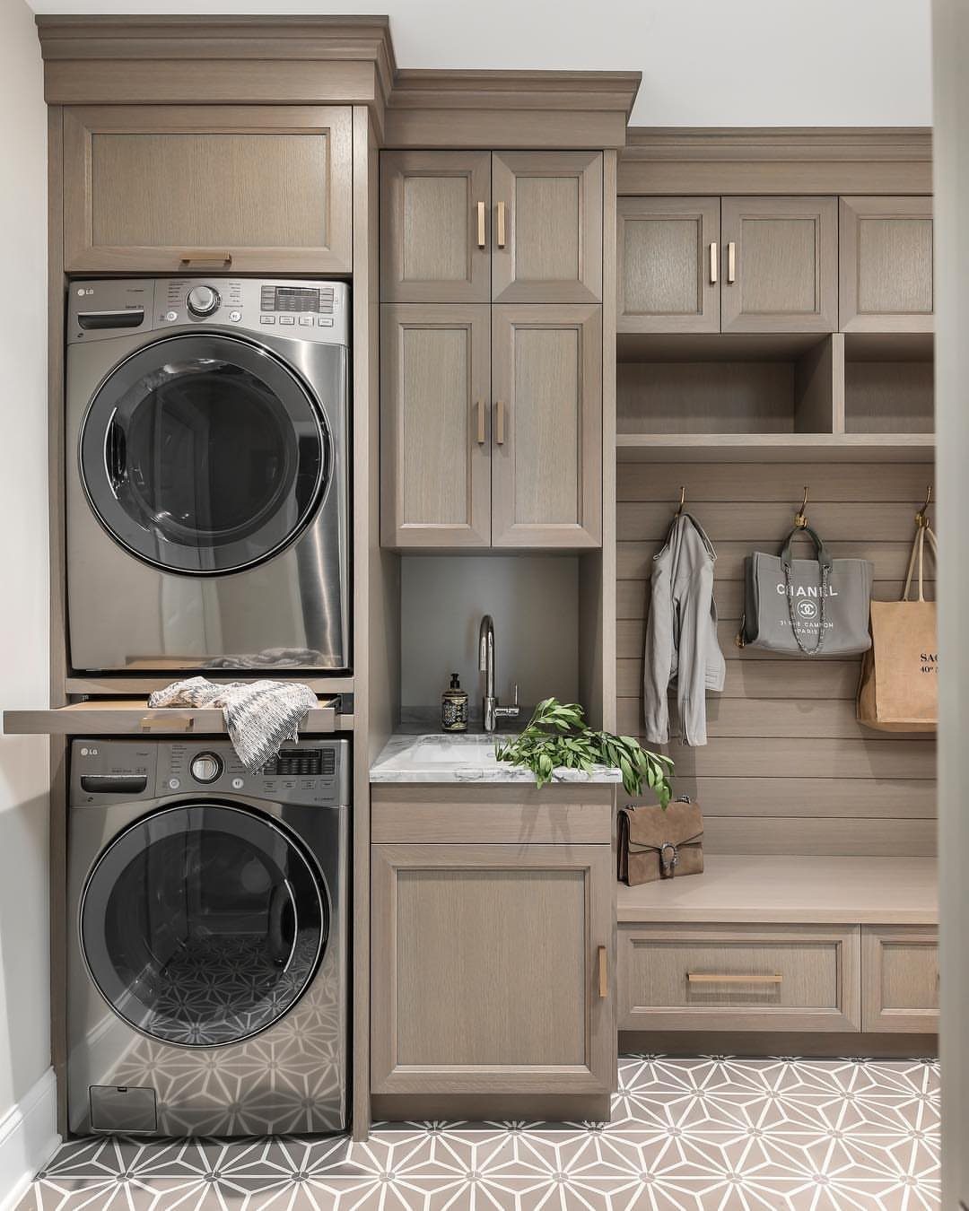 Stacked washer and dryer next to a sink and a bench with hooks.