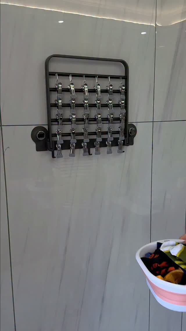 Wall-mounted drying rack with silver clips on a grey marbled tile wall.