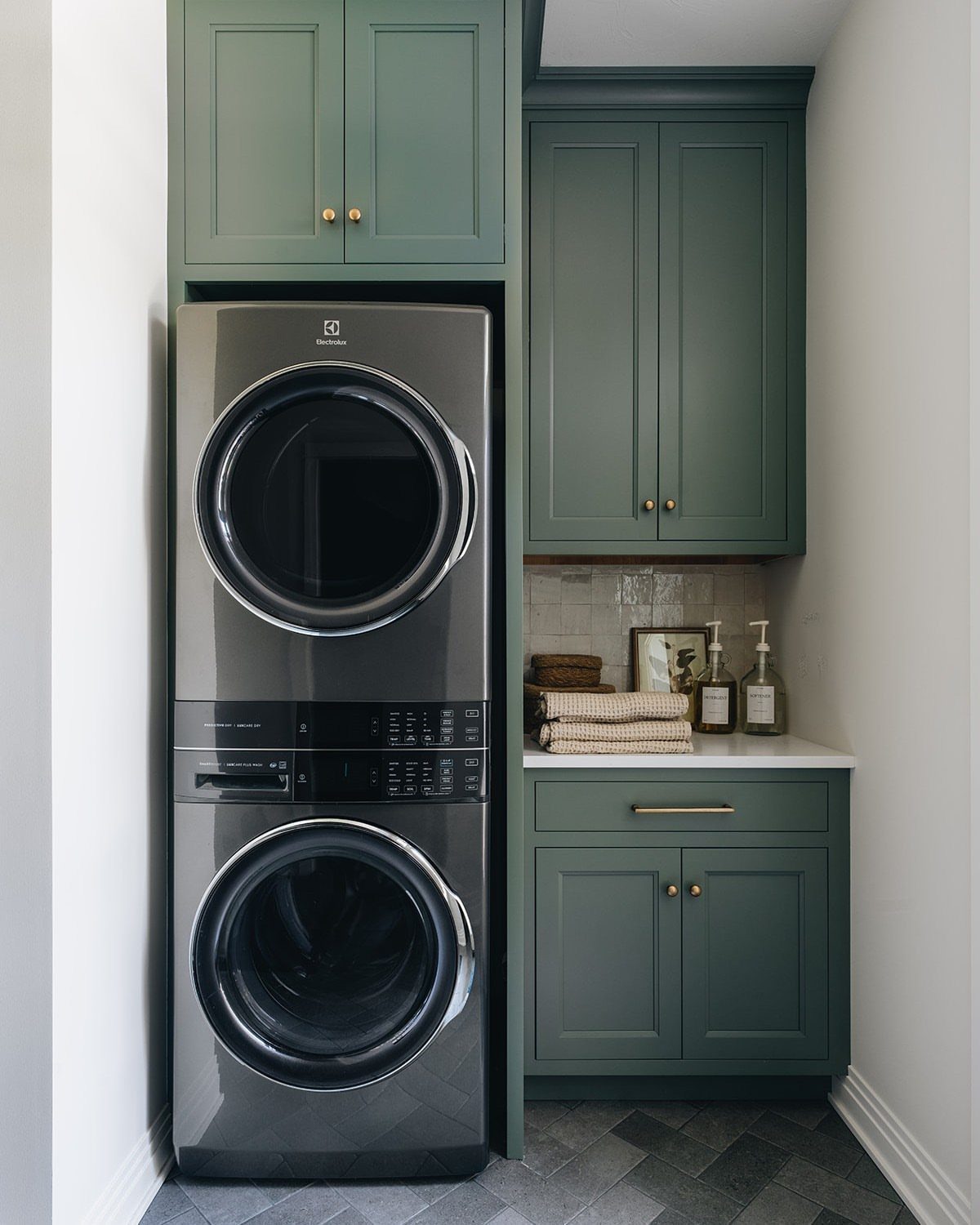 Stackable washer and dryer integrated into dark green laundry room cabinetry with counter space.