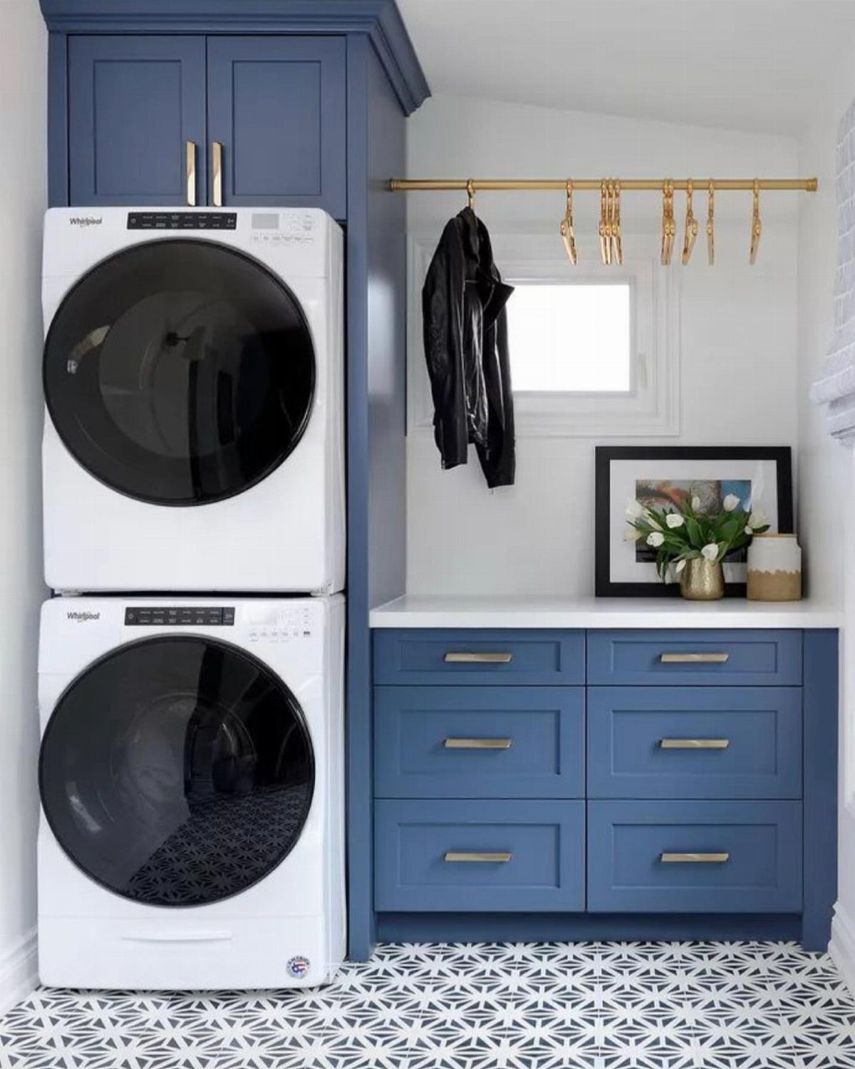 Stackable washer and dryer in a navy blue cabinet with matching laundry drawers.