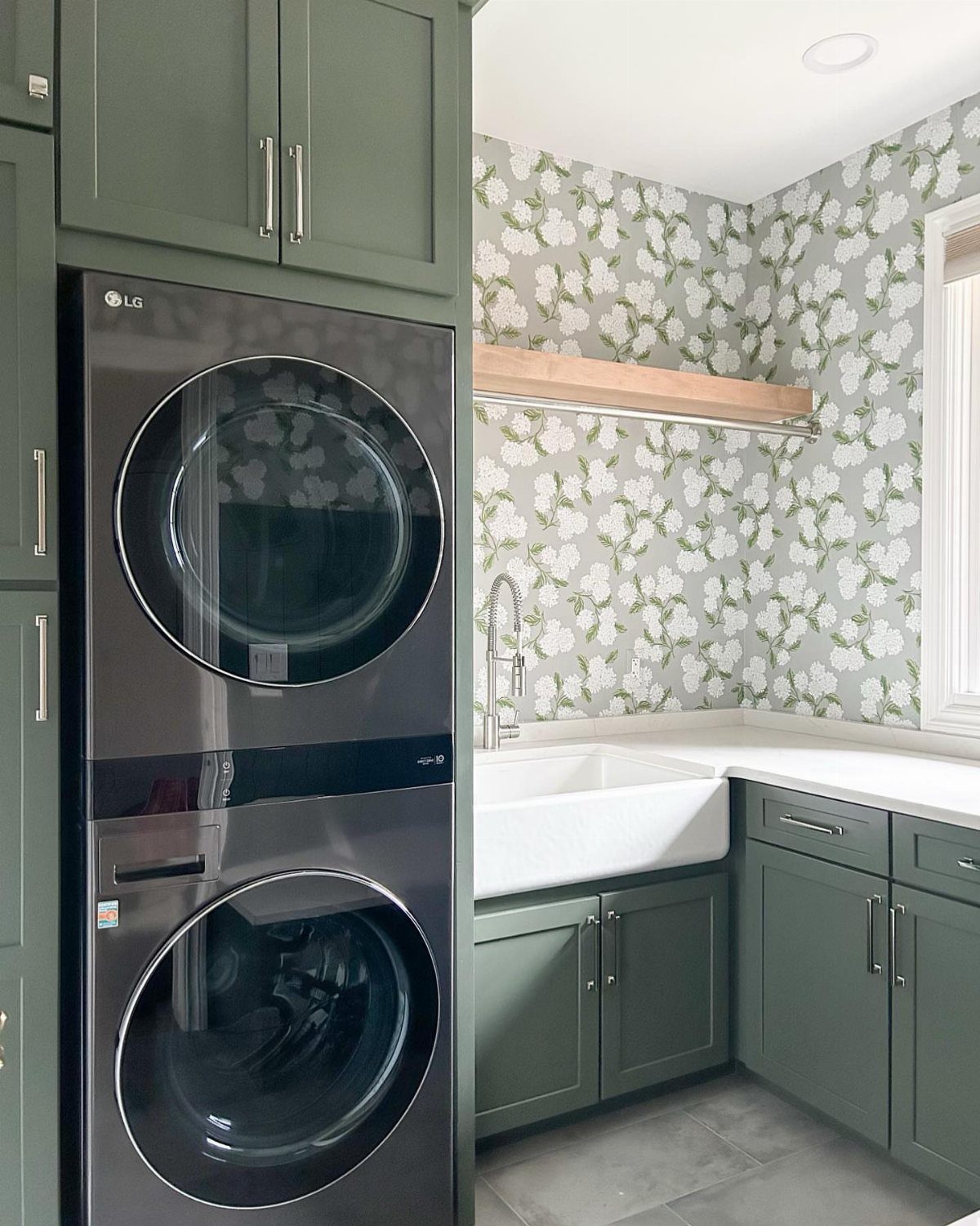 Stacked black washer and dryer next to a sink with floral wallpaper walls.