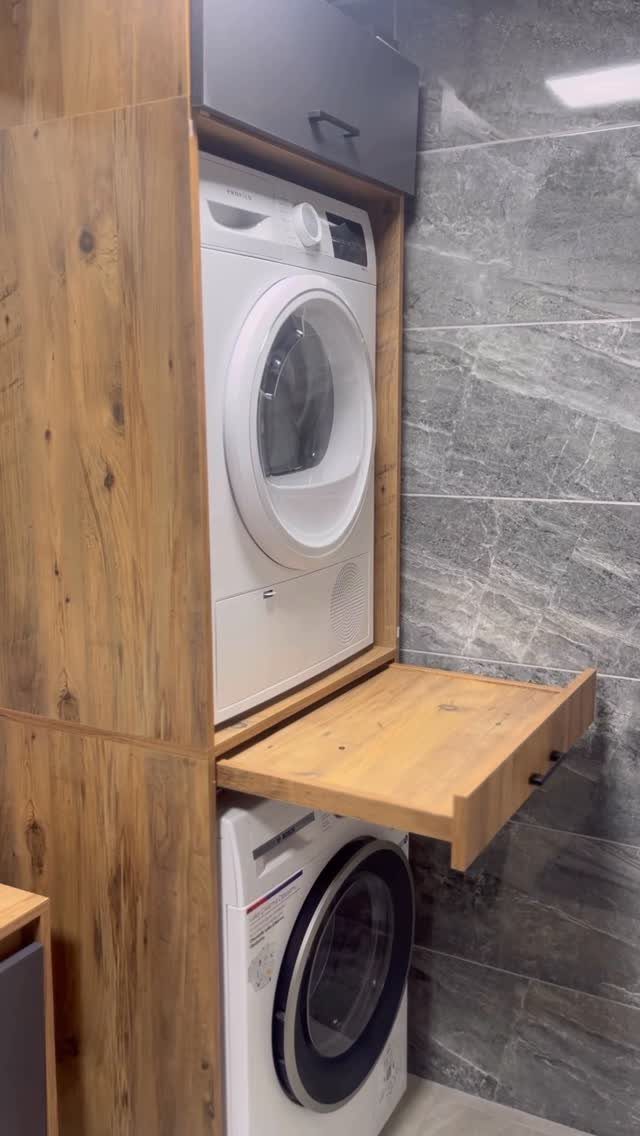 Stacked washer and dryer in wood cabinetry with a pull-out wooden shelf