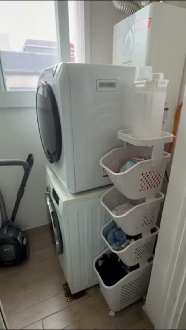 Stacked white washer and dryer next to a rolling four-tier laundry basket organizer.