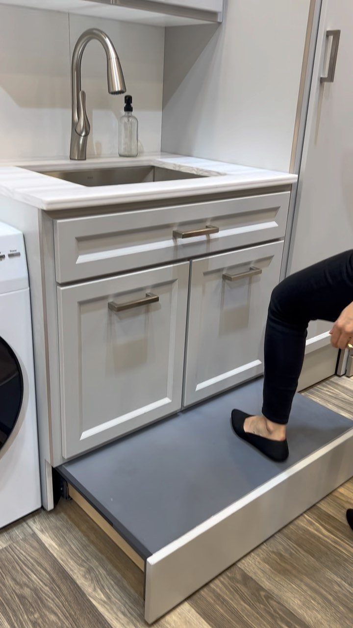 Grey pull-out step stool beneath a laundry room cabinet with a person stepping up.