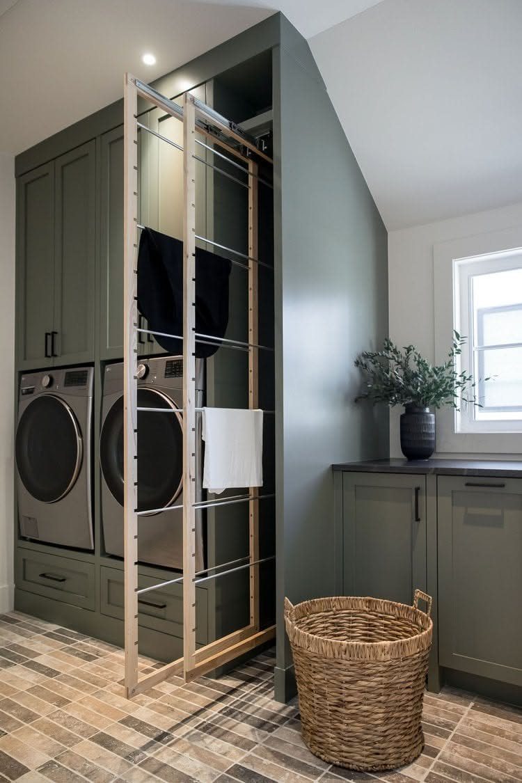 Sage green laundry room with side-by-side washers and a wooden pull-out drying rack.