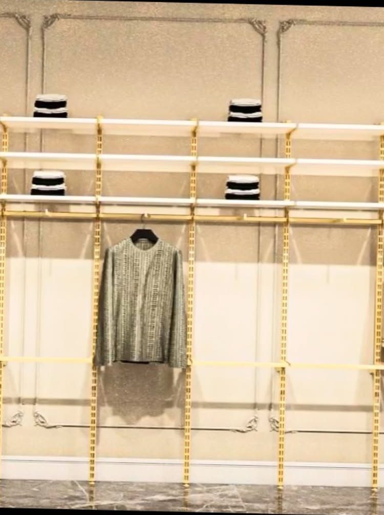 White adjustable shelving and gold hanging rods with a grey jacket and boxes.