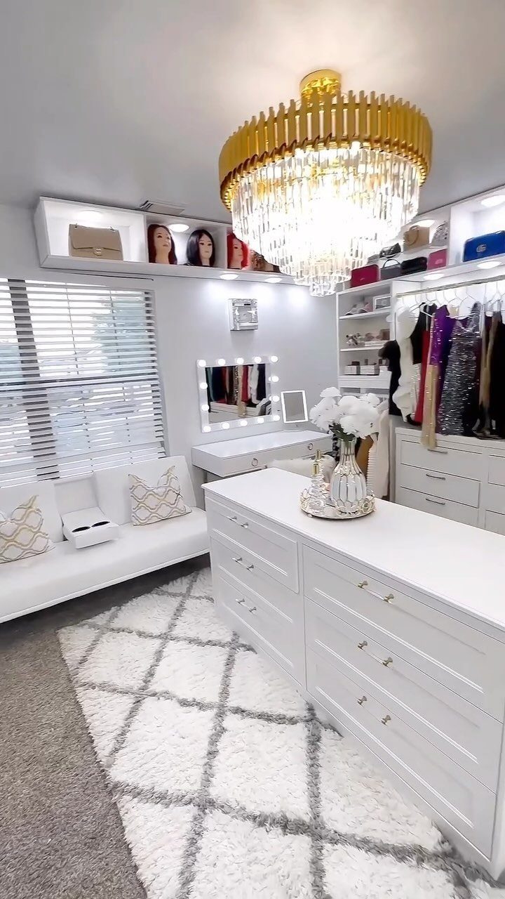 White walk-in closet room with a gold chandelier, vanity, and clothing racks.