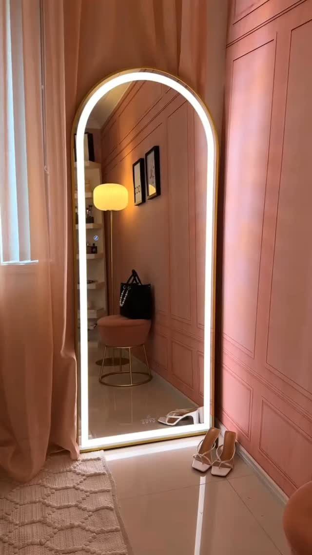 Arched full-length mirror with LED lighting against a pink paneled wall with shoes.
