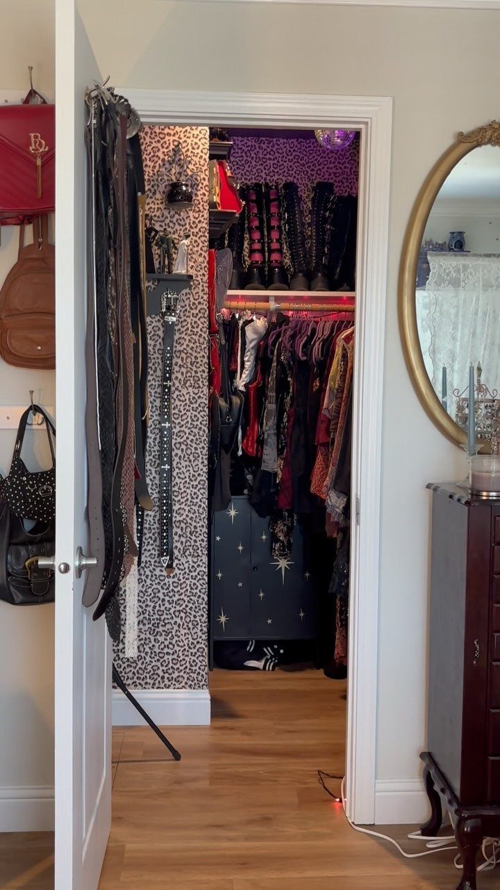 Walk-in closet with leopard print accent wall, hanging clothes, and black boots.