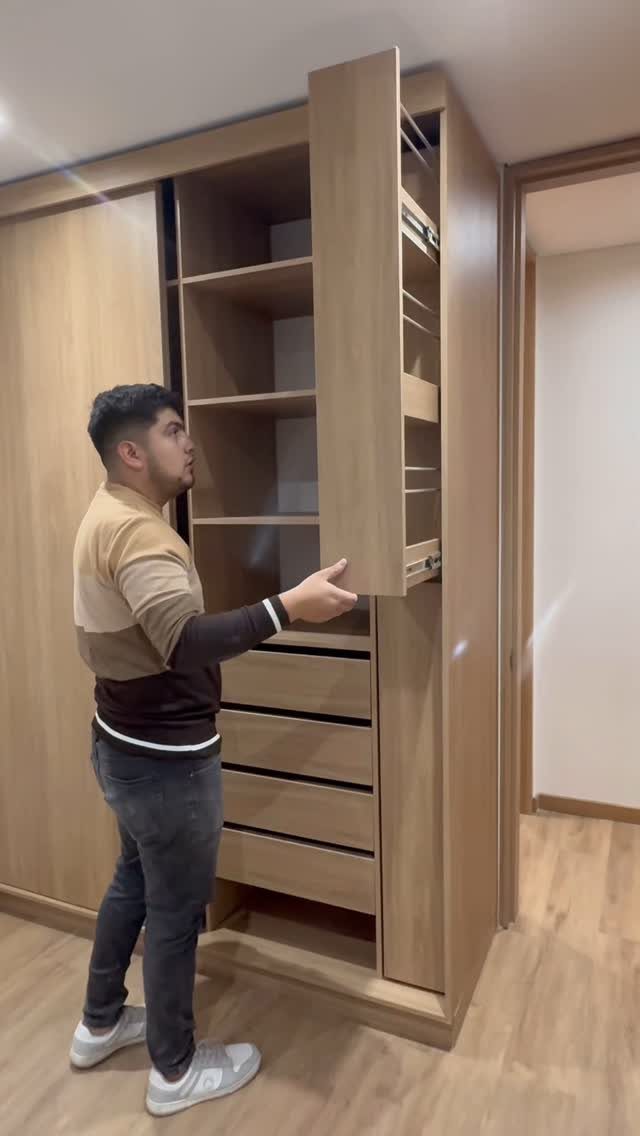 Man opening a light-wood built-in closet with pull-out drawers and door organizers.