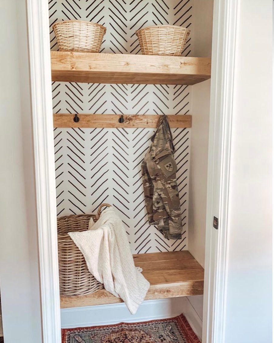 Converted closet mudroom with wooden shelves, black hooks, and a wooden bench seat.