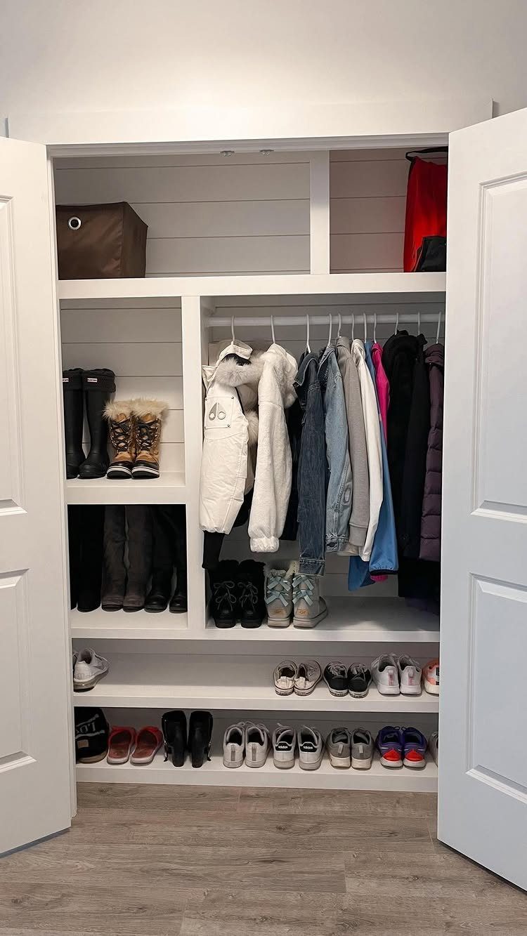 White built-in closet mudroom with organized shelves for shoes and hanging winter coats.