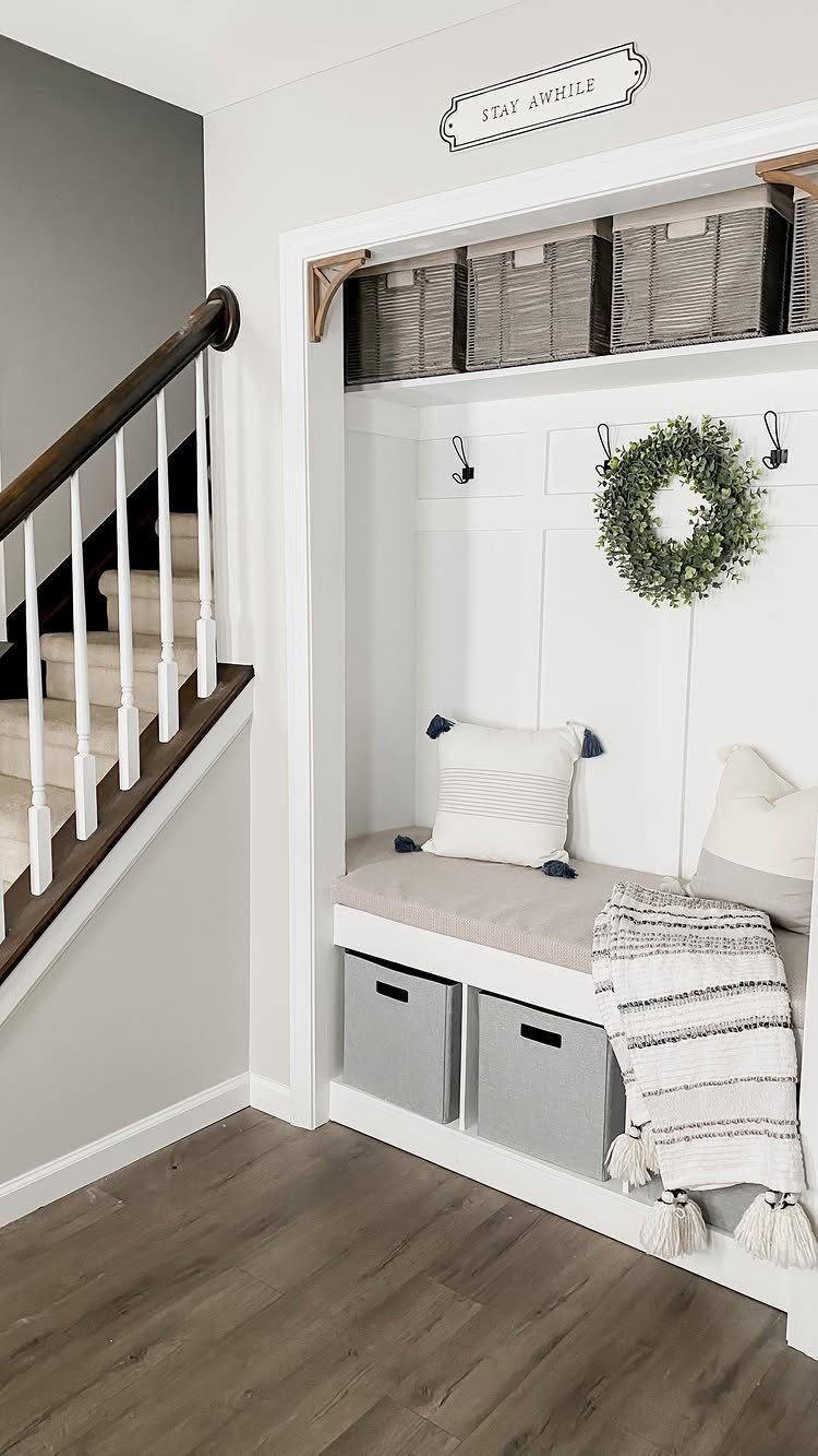 White mudroom nook with grey storage bins under a bench and wire baskets above.