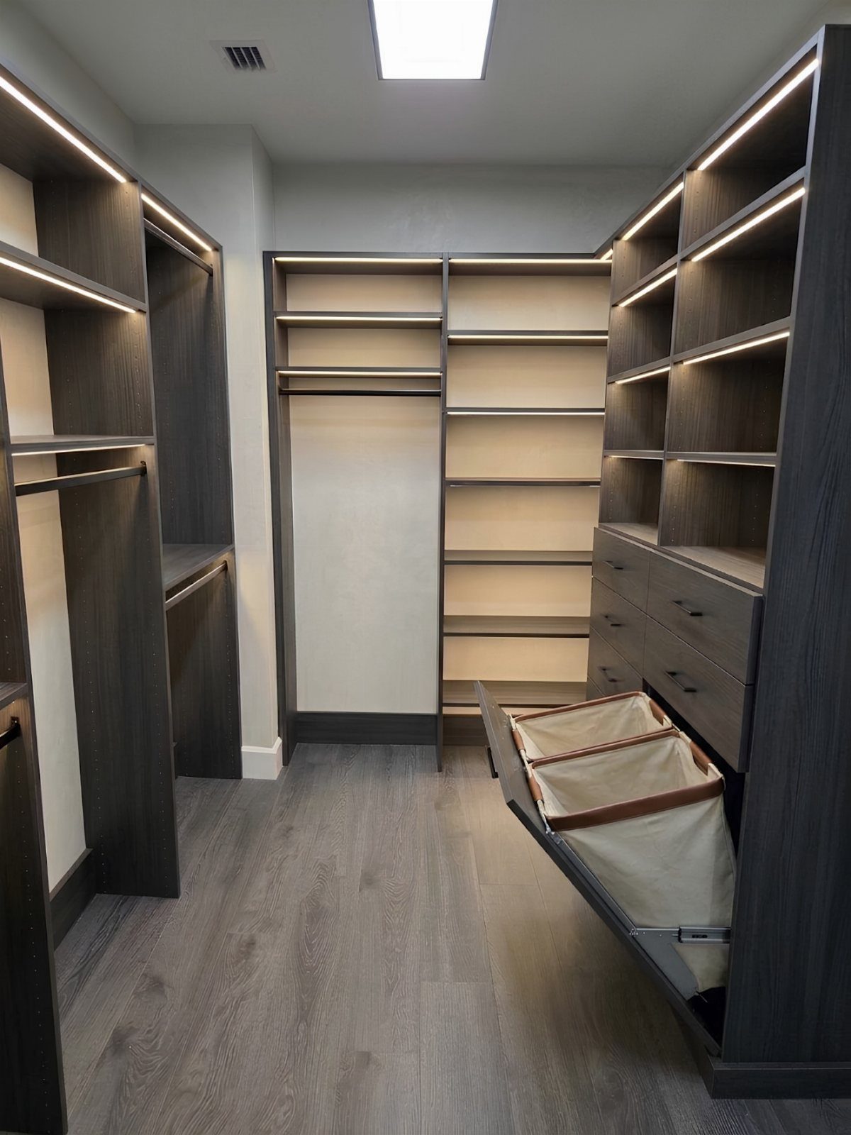 Modern walk-in closet with dark grey shelving and a pull-out built-in laundry hamper.