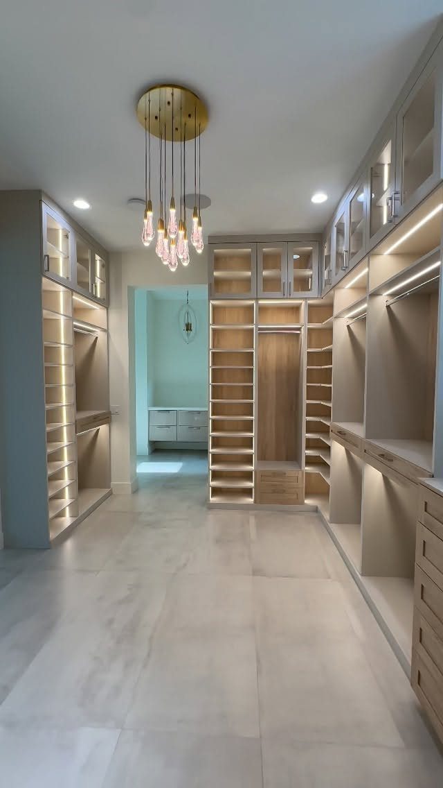 Modern walk-in closet with floor-to-ceiling shelving, integrated lighting, and a gold chandelier.