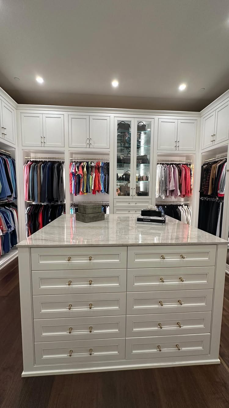 Large white walk-in closet with a marble island and organized clothing storage.