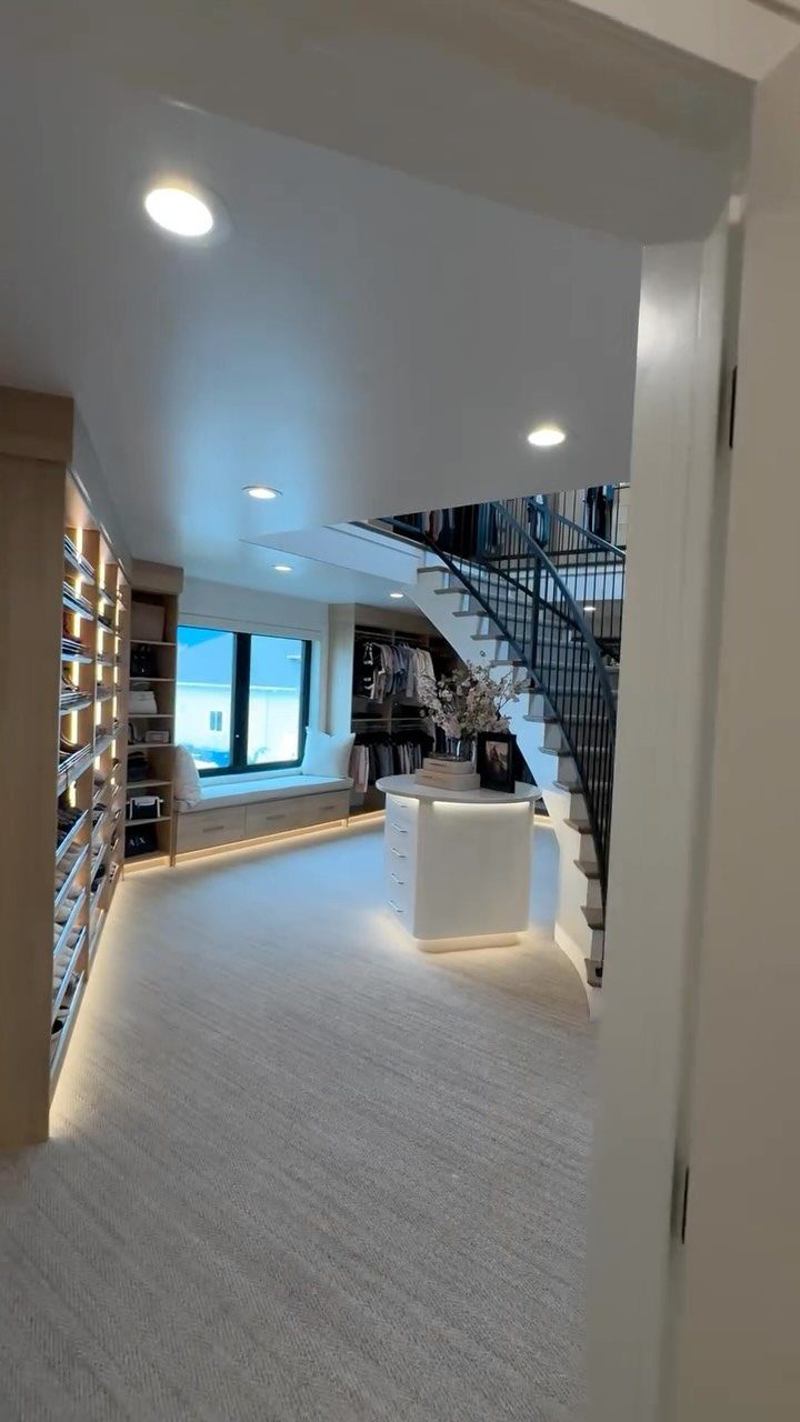 Large modern walk-in closet with white carpet, built-in shelving, and a spiral staircase.