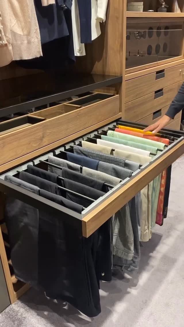 Pull-out wooden rack in a closet holding several pairs of folded trousers.