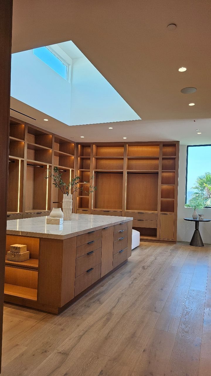 Large walk-in closet with light wood shelving, central island, and a bright skylight.