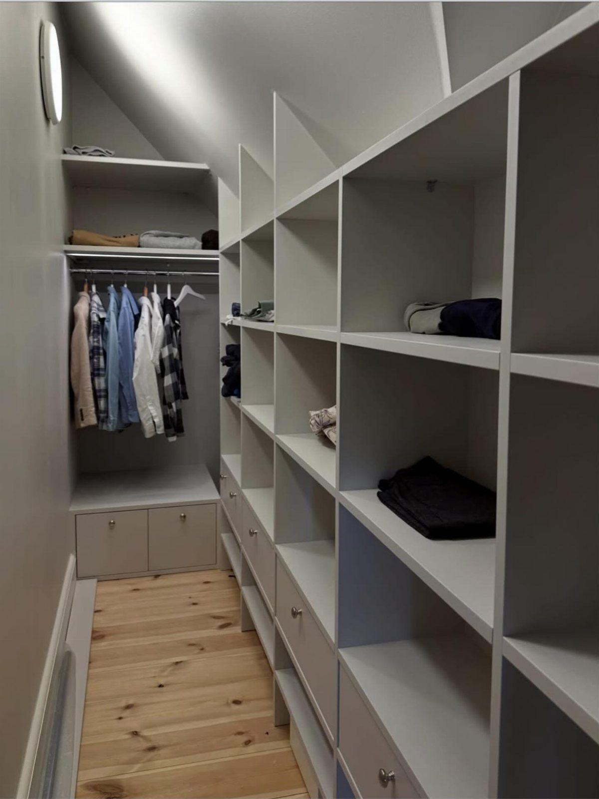 Large walk-in closet with white built-in shelves, hanging clothes, and light wood flooring.