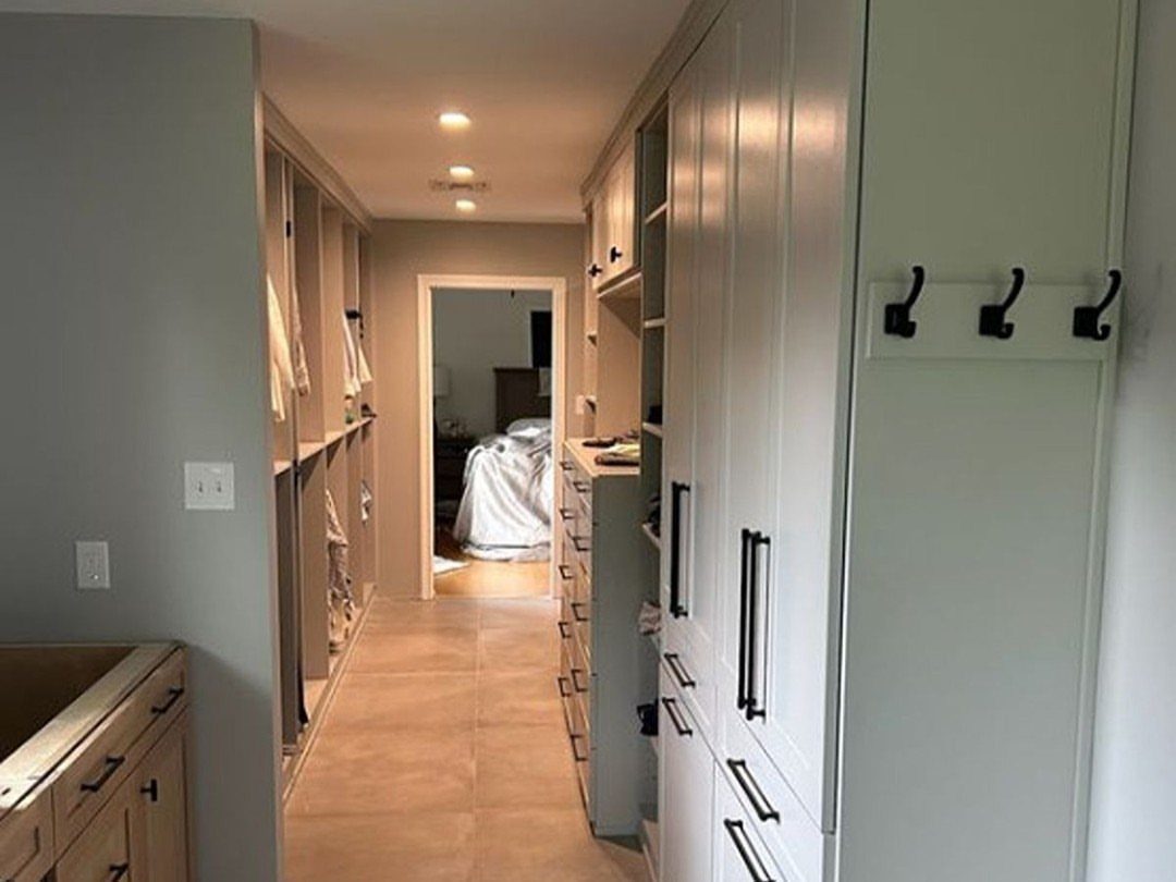 Three black wall hooks mounted on a white cabinet in a large walk-in closet.