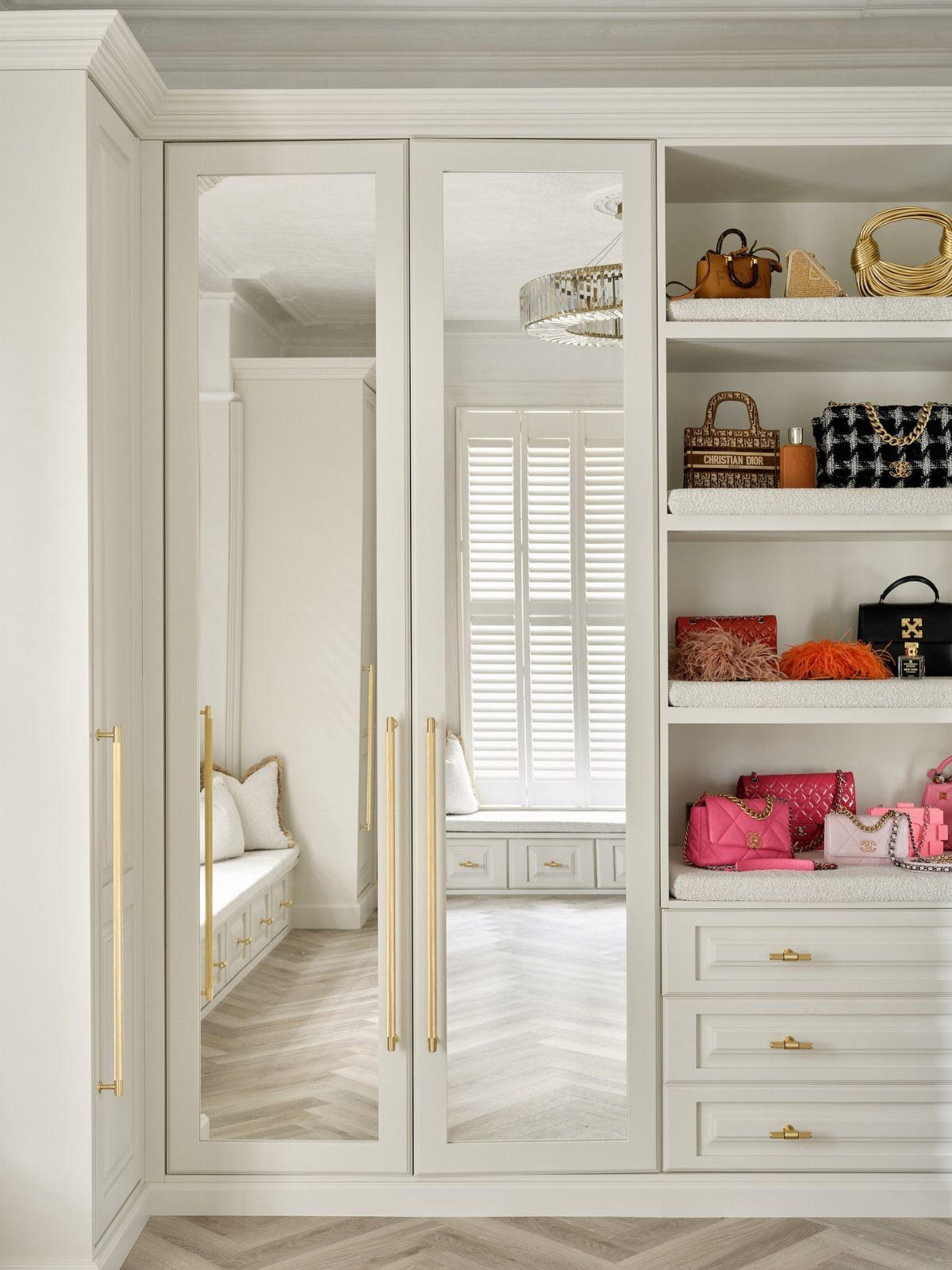 Mirrored closet doors with gold handles next to white shelves with luxury handbags.