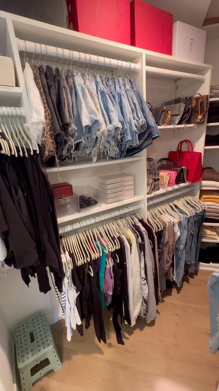 White walk-in closet with double hanging rods and top-shelf storage boxes.