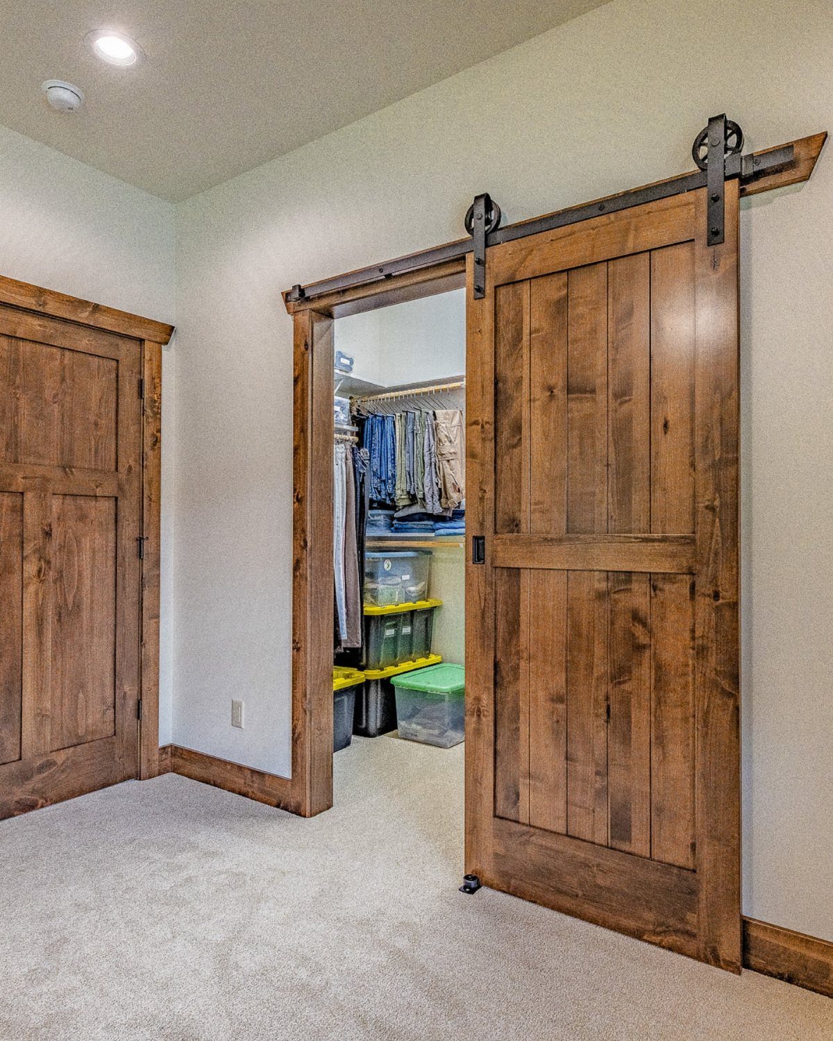 Wooden barn door sliding open to reveal a walk-in closet with organized clothing.