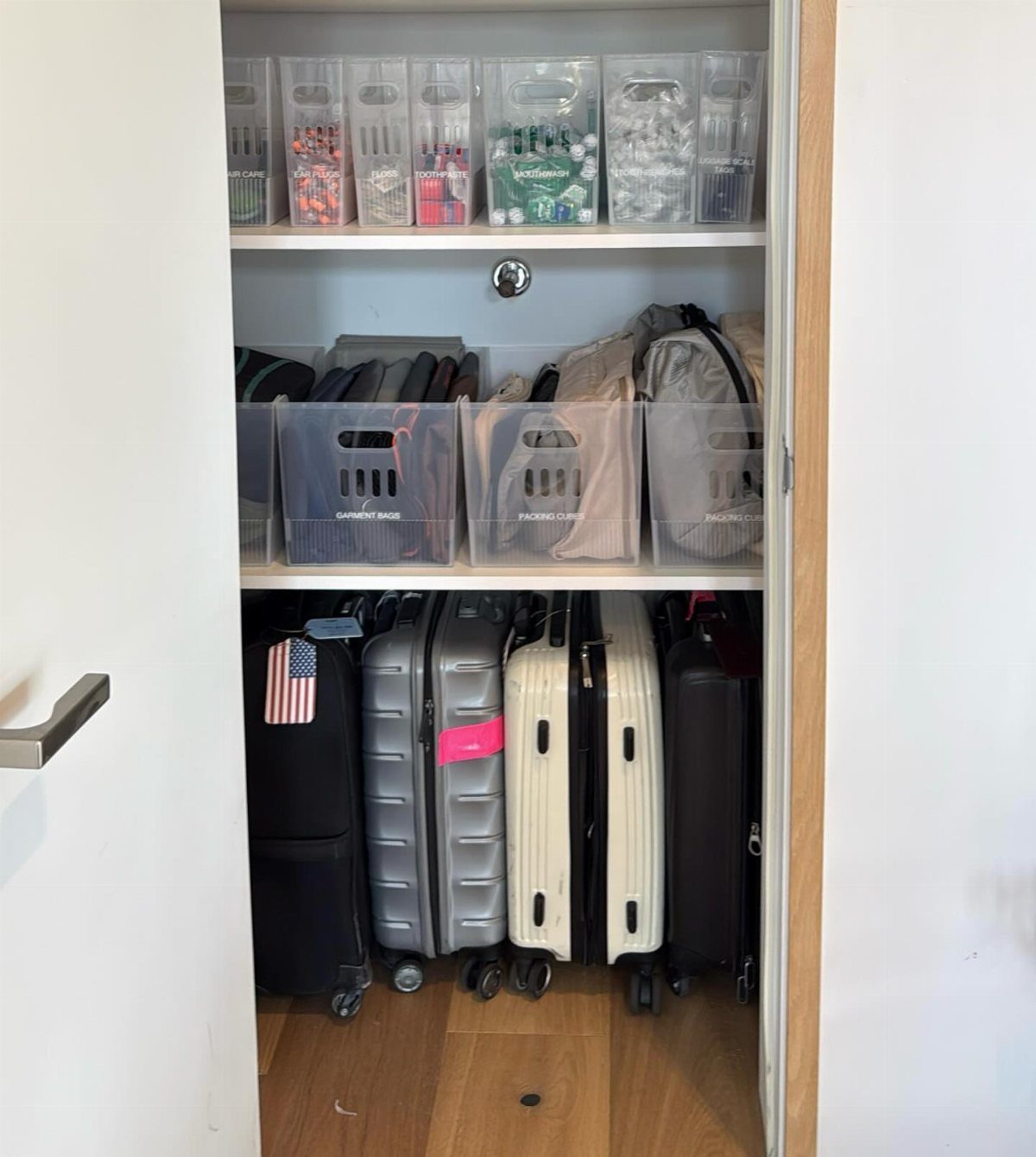 White closet shelves with clear plastic storage bins and suitcases on the floor.