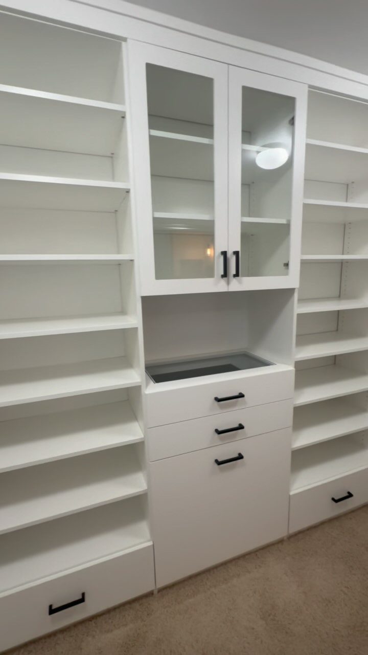White built-in closet system with open shelves, glass cabinets, and black drawer handles.