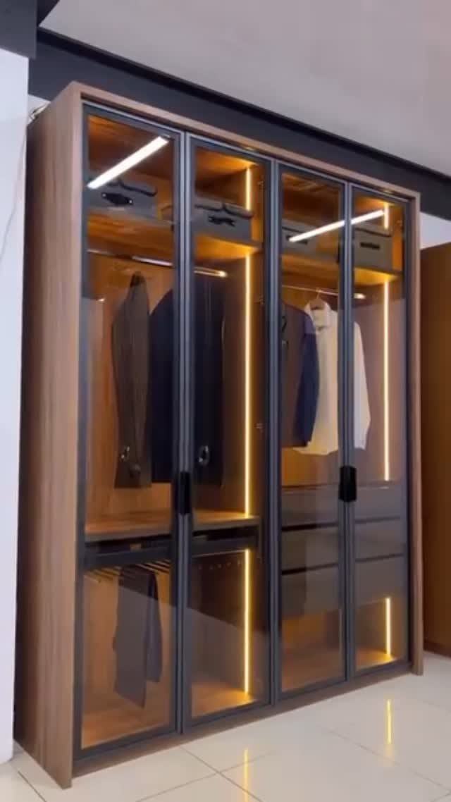 Modern wooden wardrobe with glass doors, integrated lighting, and hanging suits inside.