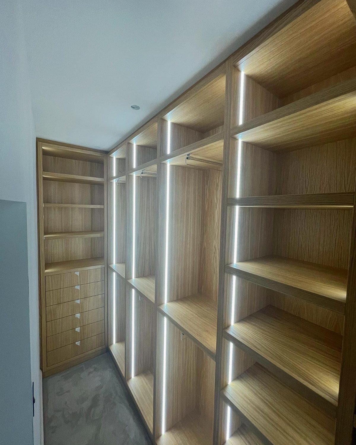 Light wood walk-in closet with integrated vertical LED strip lighting on shelves