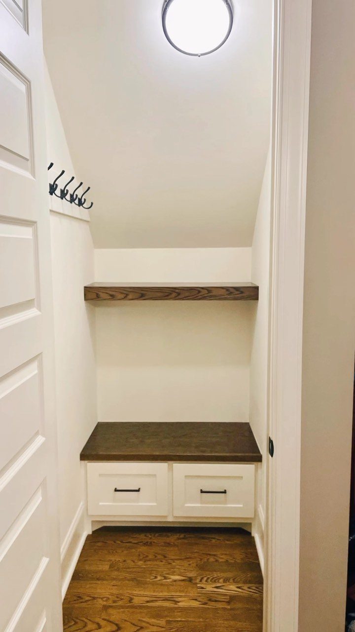 Sloped ceiling in a small white walk-in closet with wooden shelving and dresser.