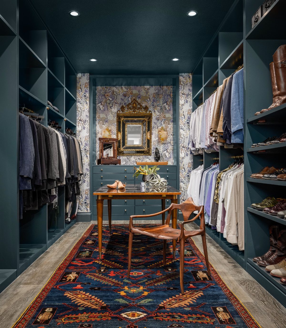 Deep teal walk-in closet with a wooden desk, leather chair, and ornate rug.