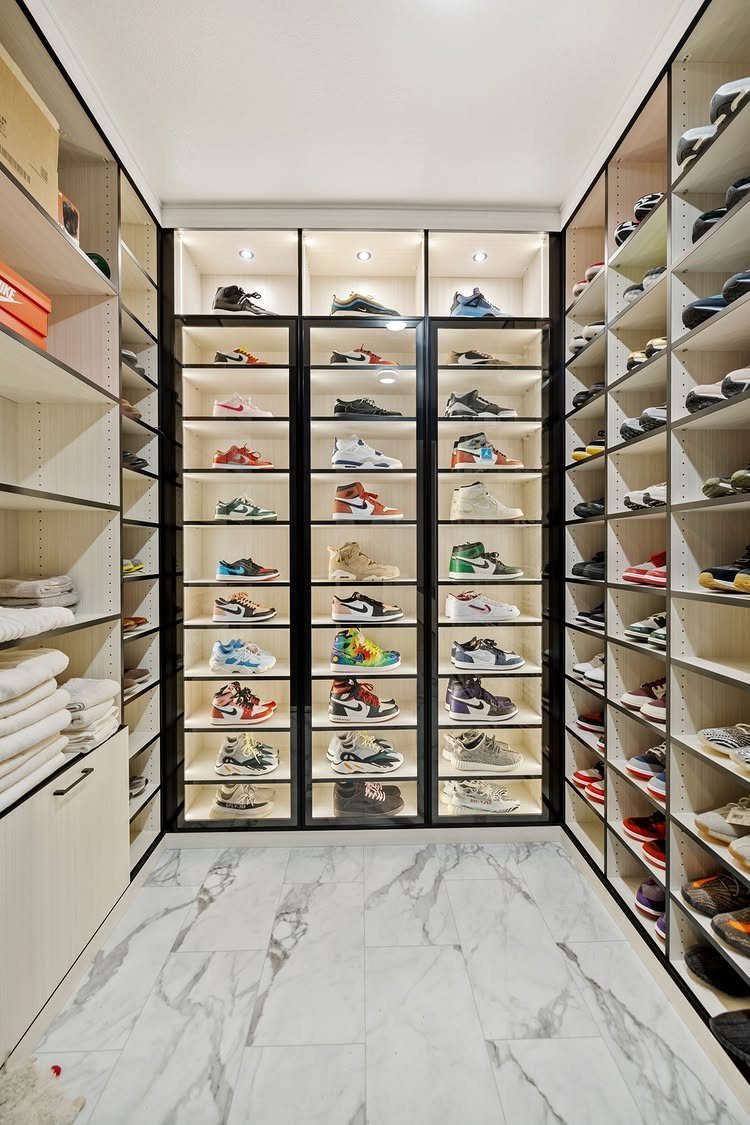 Sneakers displayed on illuminated shoe shelves in a modern white walk-in closet.