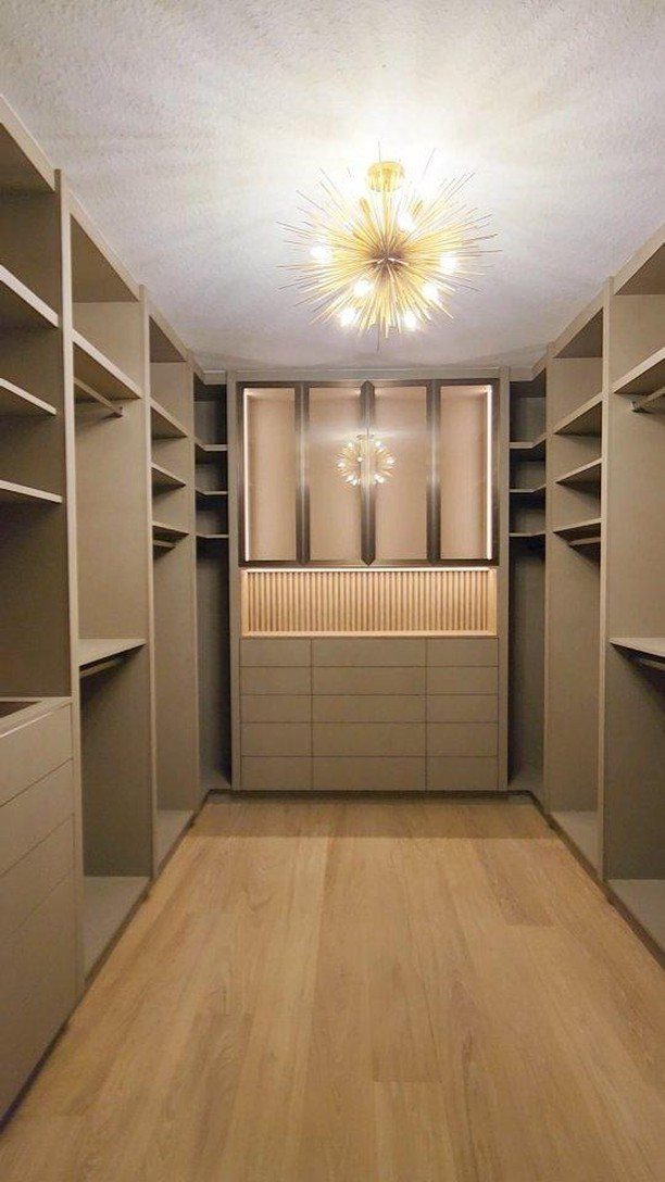Luxurious walk-in closet with beige shelving, wood floors, and a gold starburst chandelier.