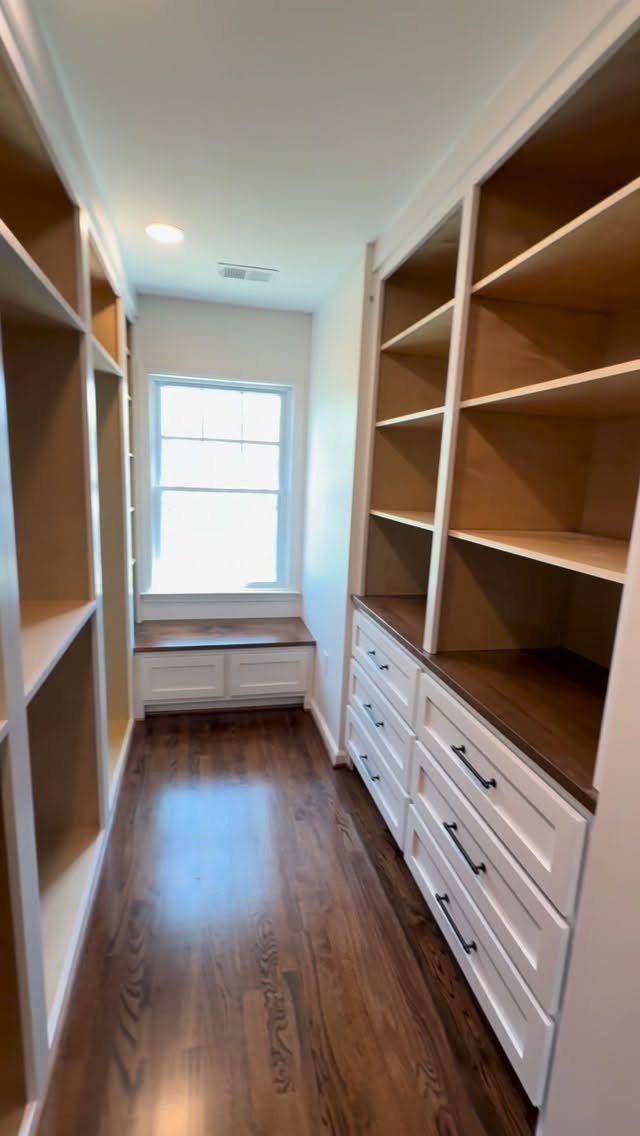 White built-in closet shelving and drawers lining a narrow hallway with wooden floors.