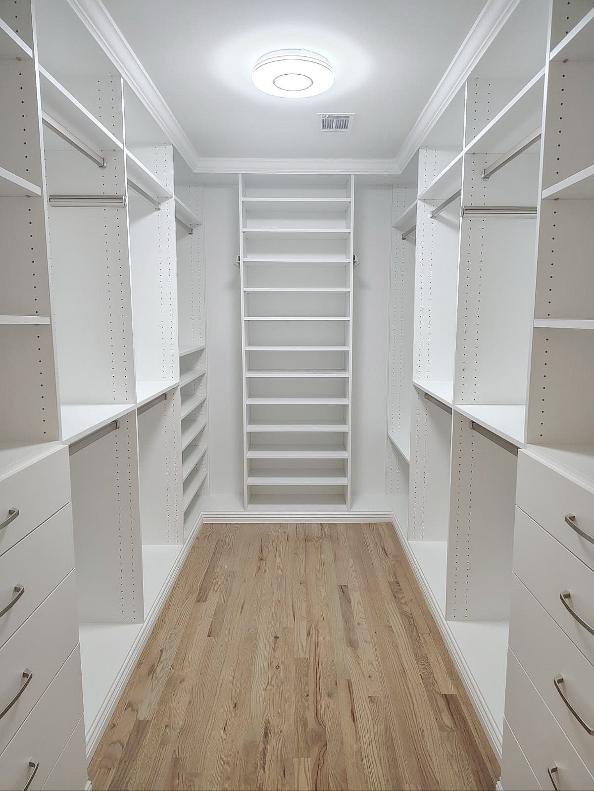 White walk-in closet with built-in shelving, hanging rods, and light wood flooring.