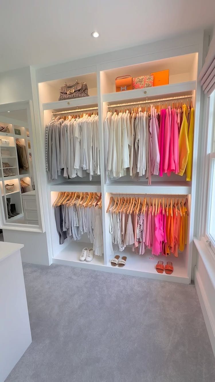 White walk-in closet with double-hang rods and clothes organized by color.
