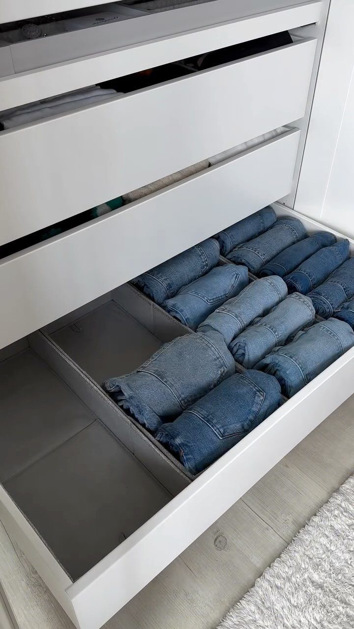 White closet drawer with grey dividers organizing rolled blue jeans for efficient storage.