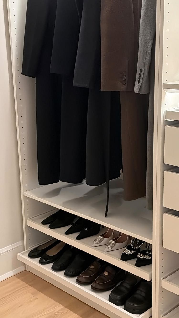 White closet system with hanging blazers and open shelves for shoes.