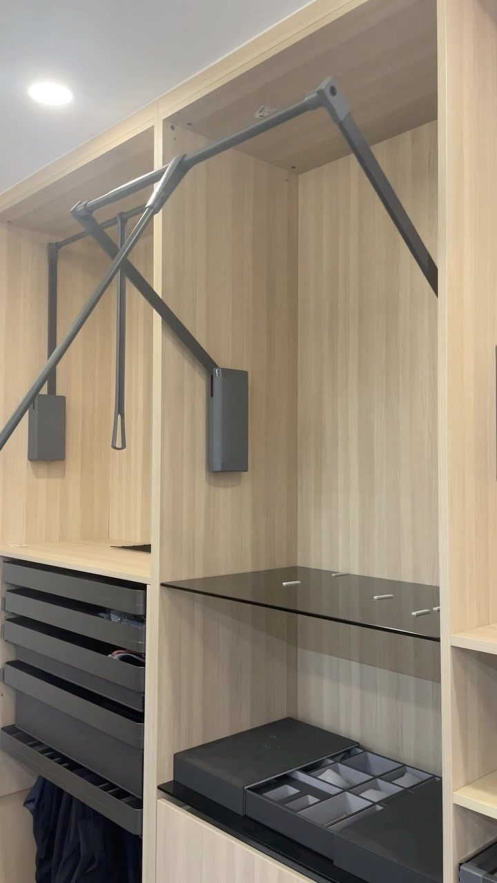 Light wood closet with a grey pull-down wardrobe lift and organized storage drawers.