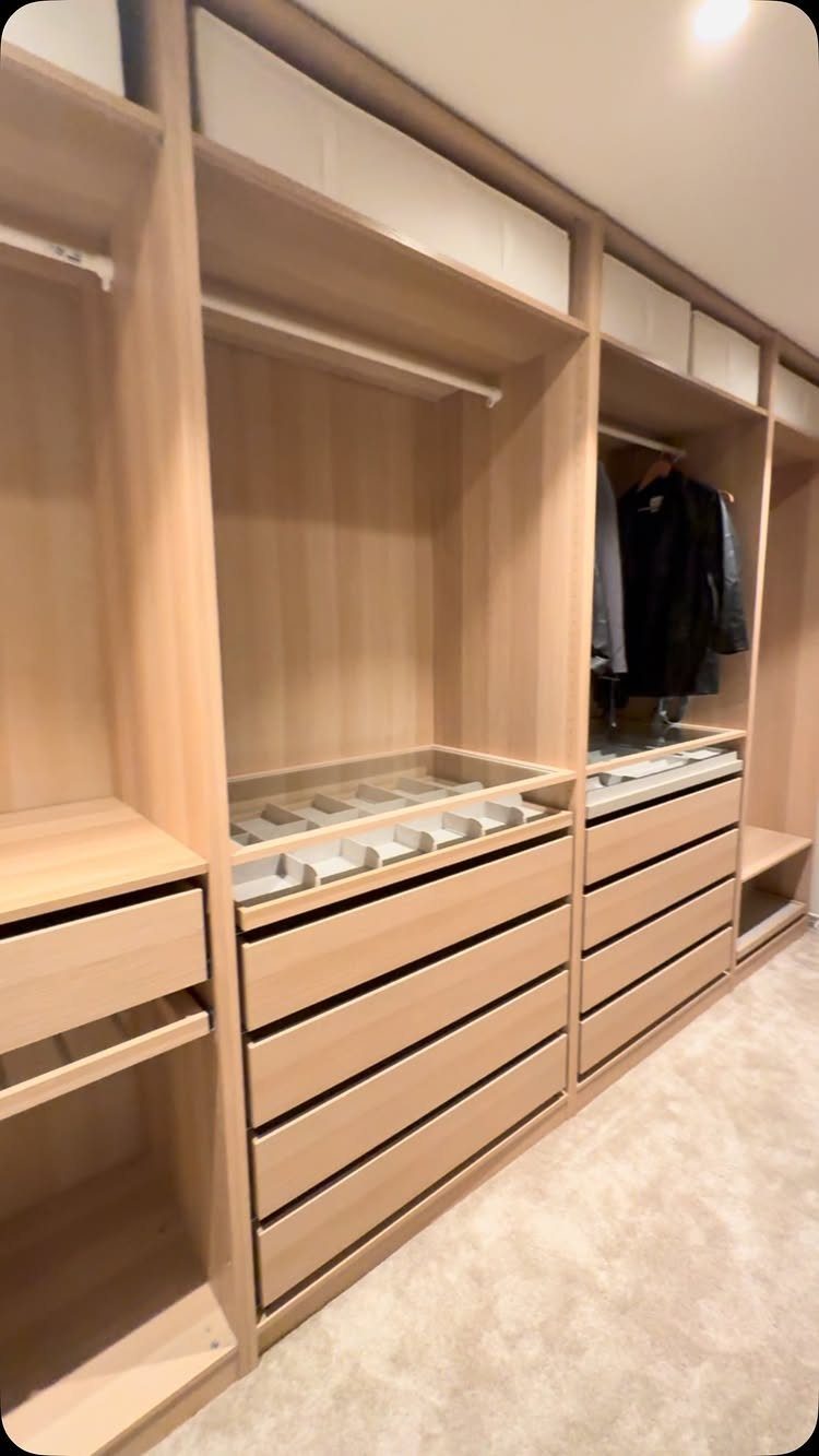 Light wood walk-in closet with drawers and hanging rods along one wall.