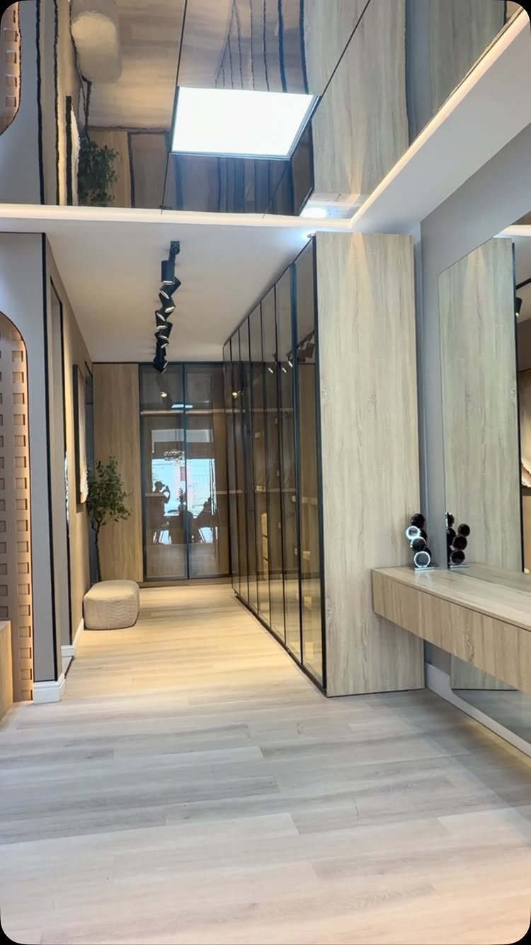 Modern interior hallway with light wood paneling, glass cabinets, and light flooring.
