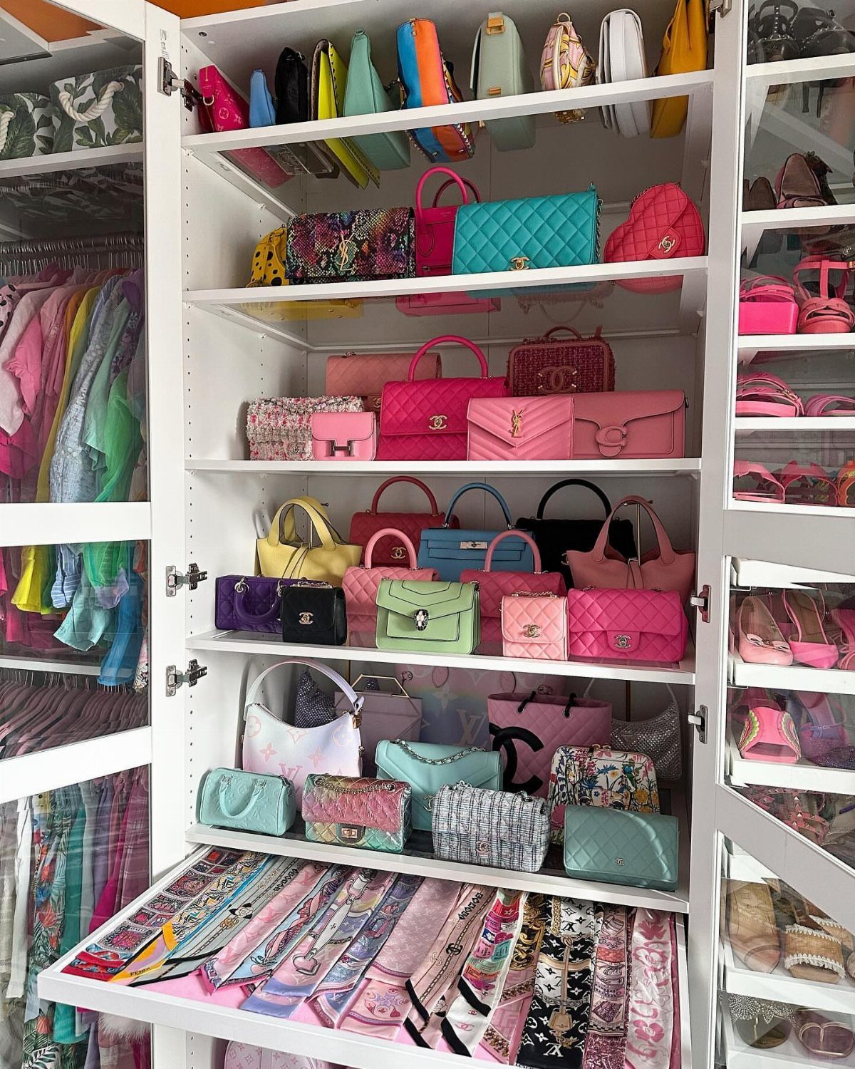 Colorful designer handbags organized on white shelves in a bright walk-in closet.